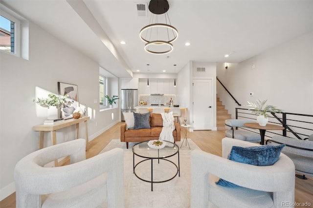 living area with stairway, light wood-type flooring, visible vents, and a healthy amount of sunlight