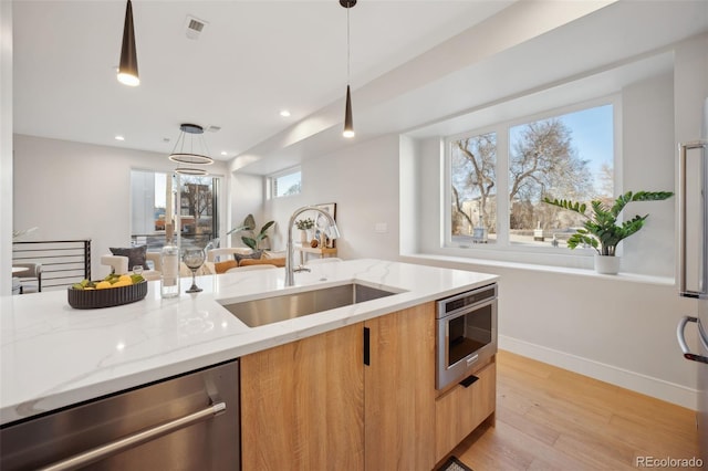 kitchen with light stone counters, stainless steel dishwasher, a sink, modern cabinets, and light wood-type flooring