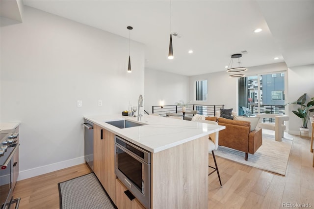 kitchen featuring light wood-style flooring, modern cabinets, appliances with stainless steel finishes, light brown cabinets, and a sink