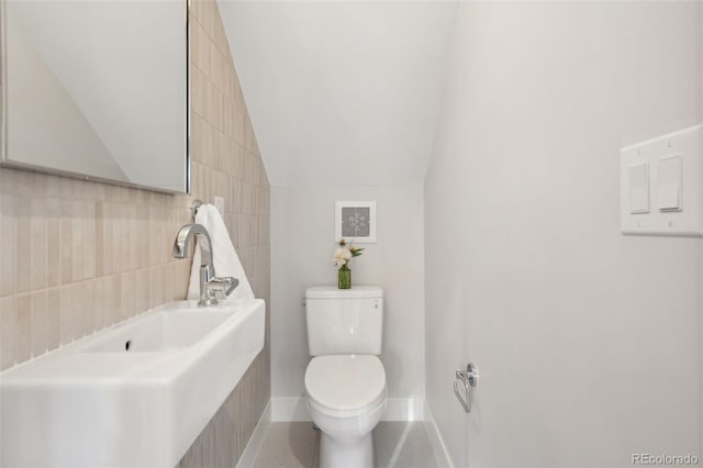 half bathroom featuring lofted ceiling, toilet, a sink, visible vents, and baseboards