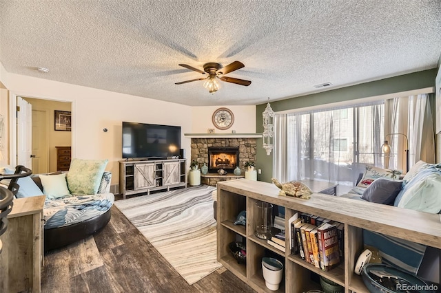 living room with wood-type flooring, a stone fireplace, a textured ceiling, and ceiling fan