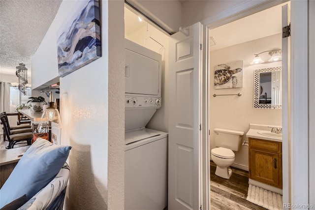 laundry room featuring stacked washer / dryer, sink, a textured ceiling, and light hardwood / wood-style flooring