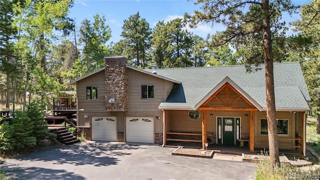 rustic home featuring a shingled roof, a chimney, a garage, and aphalt driveway