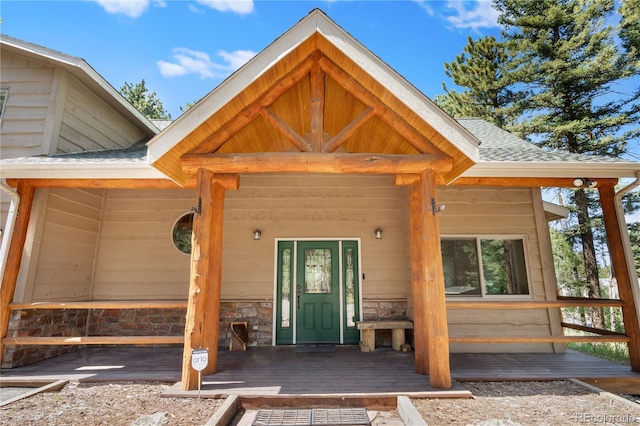 view of exterior entry featuring stone siding, a shingled roof, and covered porch