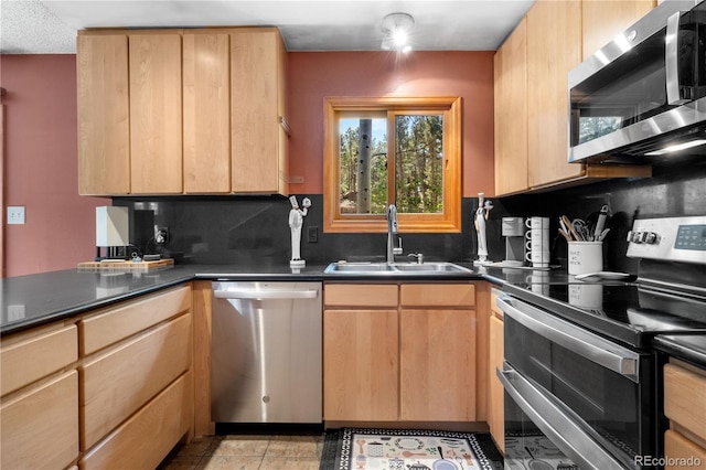 kitchen featuring light tile patterned floors, dark countertops, appliances with stainless steel finishes, a sink, and backsplash