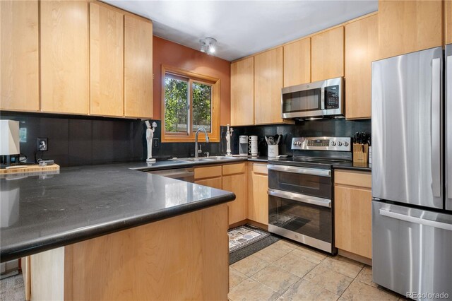 kitchen with appliances with stainless steel finishes, dark countertops, light brown cabinets, and a sink