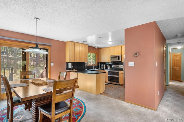 kitchen featuring light carpet, dark countertops, appliances with stainless steel finishes, light brown cabinets, and a sink