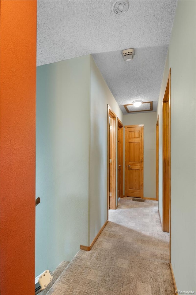 hall featuring carpet flooring, a textured ceiling, and baseboards