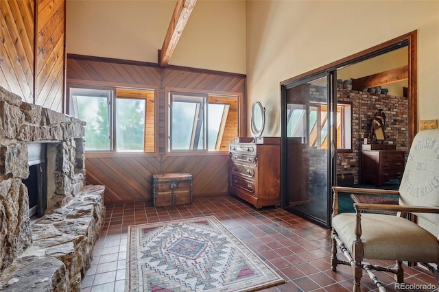 tiled living room with high vaulted ceiling, wooden walls, beam ceiling, and a stone fireplace