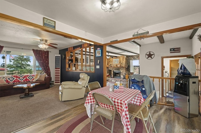 12101 Riverdale Rd, Brighton, CO 80602 - dining area featuring wood finished floors, a stone fireplace, ceiling fan, and beam ceiling