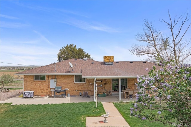 12101 Riverdale Rd, Brighton, CO 80602 - back of house featuring a lawn, brick siding, a patio, a chimney, and roof with shingles