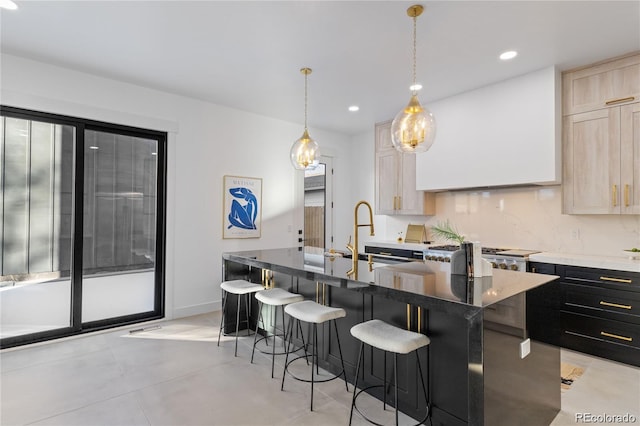 kitchen with tasteful backsplash, light brown cabinets, a kitchen bar, decorative light fixtures, and a center island with sink