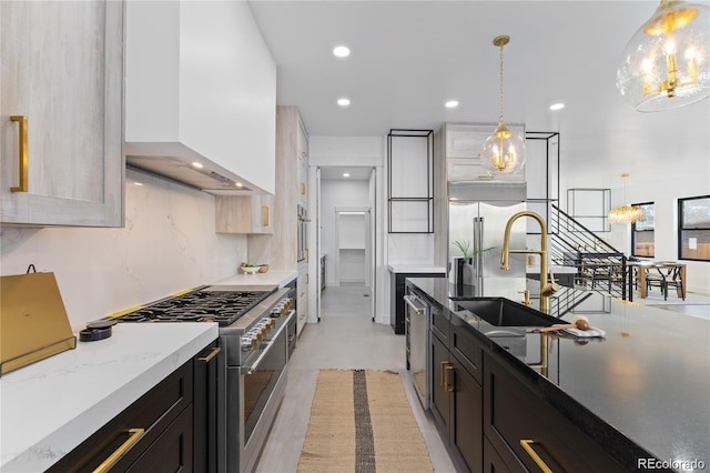 kitchen with light stone counters, sink, wall chimney range hood, appliances with stainless steel finishes, and decorative light fixtures