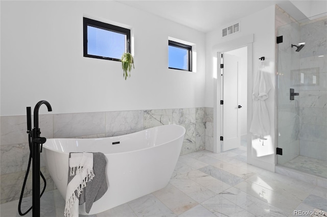 bathroom with shower with separate bathtub and tile walls