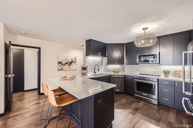 kitchen with kitchen peninsula, appliances with stainless steel finishes, decorative light fixtures, sink, and a kitchen bar