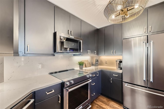 kitchen featuring light stone countertops, appliances with stainless steel finishes, gray cabinetry, tasteful backsplash, and light hardwood / wood-style flooring