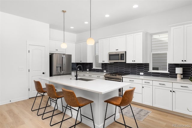 kitchen featuring white cabinetry, sink, hanging light fixtures, a kitchen island with sink, and appliances with stainless steel finishes