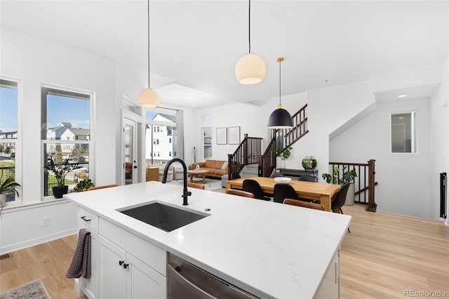 kitchen featuring stainless steel dishwasher, sink, white cabinetry, hanging light fixtures, and an island with sink