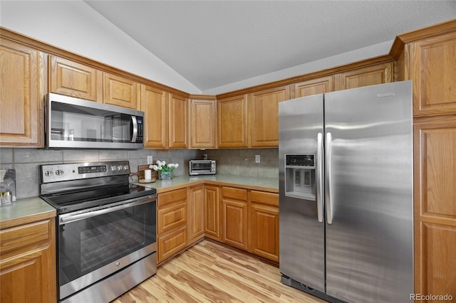 2226 Lily Dr, Loveland, CO 80537 - kitchen with stainless steel appliances, vaulted ceiling, light countertops, backsplash, and light wood-style flooring