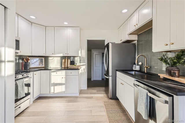 kitchen with backsplash, sink, light hardwood / wood-style flooring, appliances with stainless steel finishes, and white cabinets