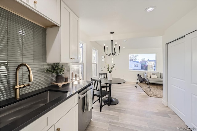 kitchen featuring stainless steel dishwasher, sink, hanging light fixtures, and white cabinetry