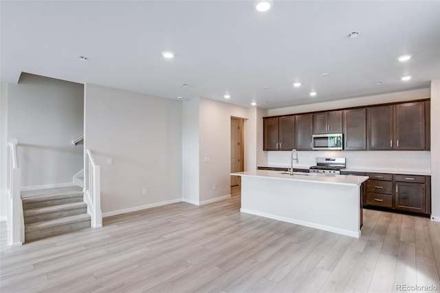1418 Hudson Pl, Longmont, CO 80501 - kitchen featuring stainless steel appliances, light wood finished floors, dark brown cabinetry, a center island with sink, and light countertops