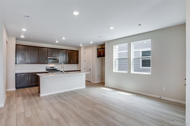 1418 Hudson Pl, Longmont, CO 80501 - kitchen with stainless steel appliances, light wood-style floors, dark brown cabinets, an island with sink, and recessed lighting