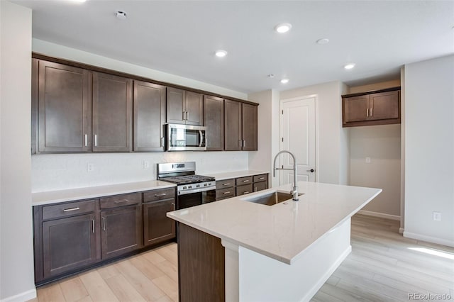1418 Hudson Pl, Longmont, CO 80501 - kitchen with stainless steel appliances, light wood-style floors, dark brown cabinets, a center island with sink, and recessed lighting