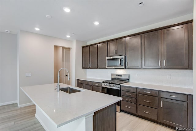 1418 Hudson Pl, Longmont, CO 80501 - kitchen with appliances with stainless steel finishes, light wood-type flooring, a kitchen island with sink, dark brown cabinets, and recessed lighting