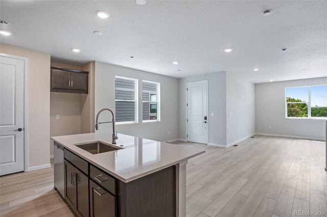 1418 Hudson Pl, Longmont, CO 80501 - kitchen featuring open floor plan, dishwasher, light wood-style floors, a kitchen island with sink, and dark brown cabinets