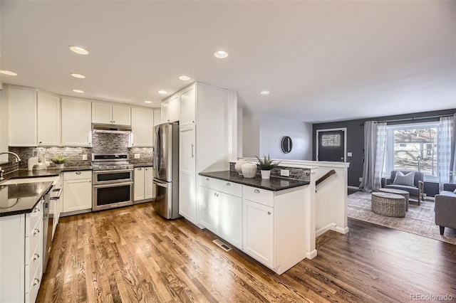 kitchen featuring appliances with stainless steel finishes, wood-type flooring, sink, white cabinets, and kitchen peninsula