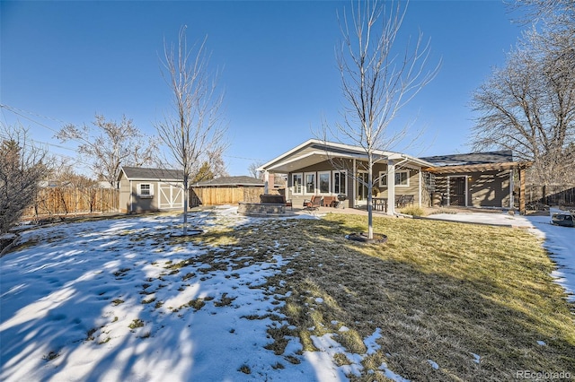 snow covered property featuring a patio, a lawn, and a storage unit