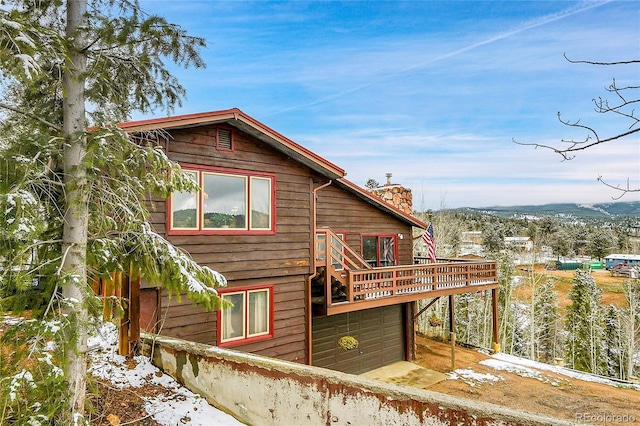 snow covered back of property featuring a garage and a wooden deck