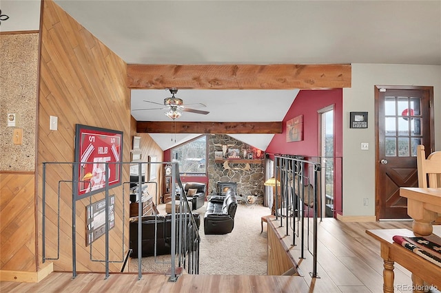 living room featuring lofted ceiling with beams, ceiling fan, light wood-type flooring, and wood walls