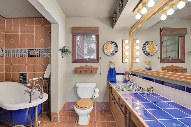 bathroom with backsplash, a tub to relax in, tile patterned flooring, vanity, and toilet