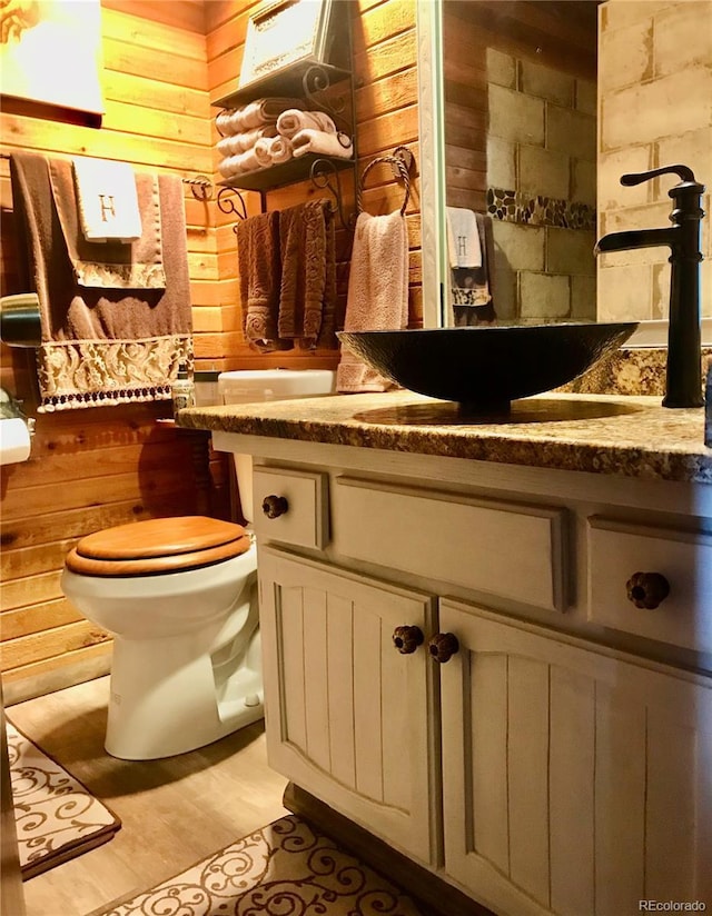 bathroom with toilet, wooden walls, sink, and hardwood / wood-style flooring