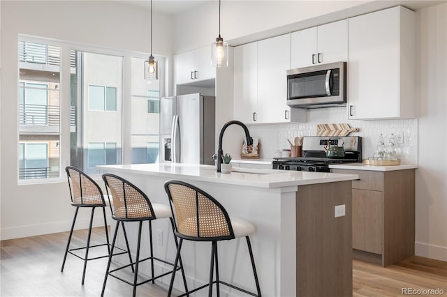 kitchen featuring a sink, light wood-style floors, appliances with stainless steel finishes, a breakfast bar area, and decorative backsplash