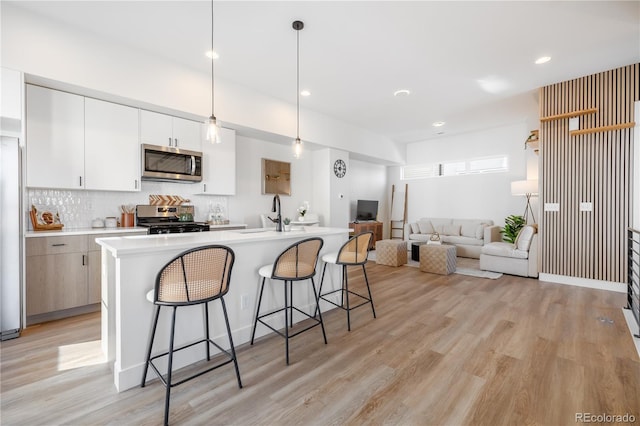 kitchen featuring light wood-type flooring, a kitchen bar, backsplash, stainless steel appliances, and light countertops