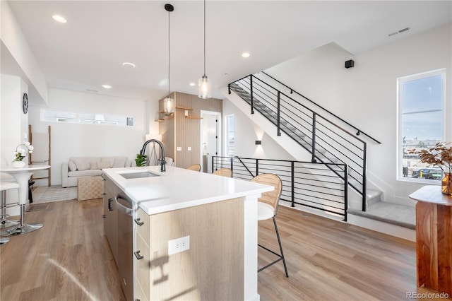 kitchen featuring a kitchen island with sink, light wood-style flooring, dishwasher, and a sink