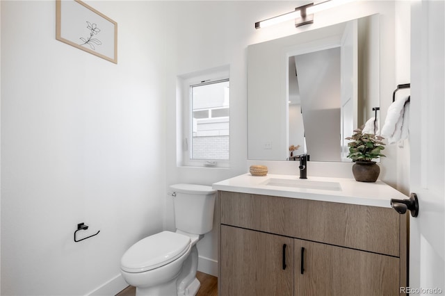 half bathroom featuring baseboards, toilet, and vanity