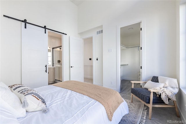 carpeted bedroom featuring visible vents, baseboards, a barn door, a closet, and ensuite bath