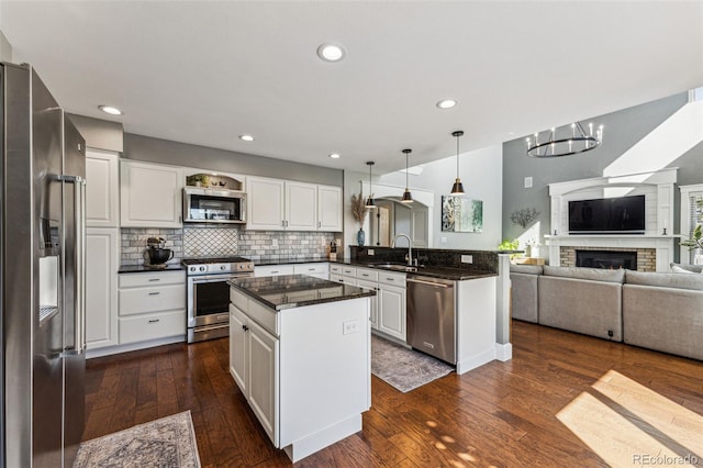 kitchen featuring stainless steel appliances, dark countertops, open floor plan, white cabinetry, and a sink