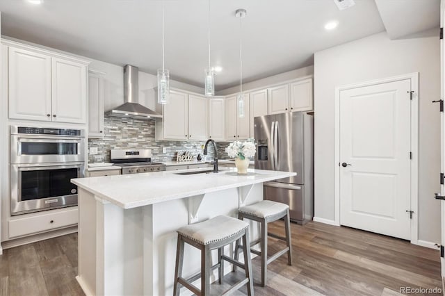 5142 N Quemoy Ct, Aurora, CO 80019 - kitchen with appliances with stainless steel finishes, wall chimney range hood, a sink, wood finished floors, and backsplash