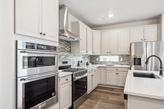 5142 N Quemoy Ct, Aurora, CO 80019 - kitchen featuring stainless steel appliances, wall chimney exhaust hood, a sink, decorative backsplash, and white cabinetry