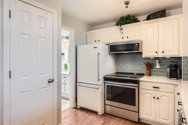 kitchen featuring decorative backsplash, white cabinets, stainless steel appliances, light countertops, and light wood-type flooring