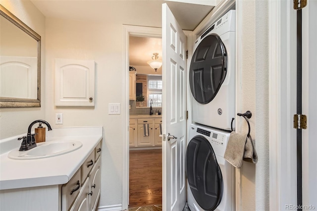 washroom featuring stacked washer and dryer, laundry area, a sink, and wood finished floors