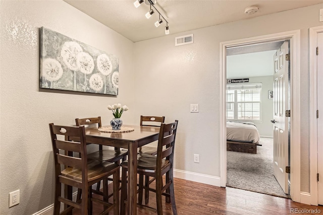 dining space featuring baseboards, visible vents, a textured wall, dark wood-type flooring, and track lighting