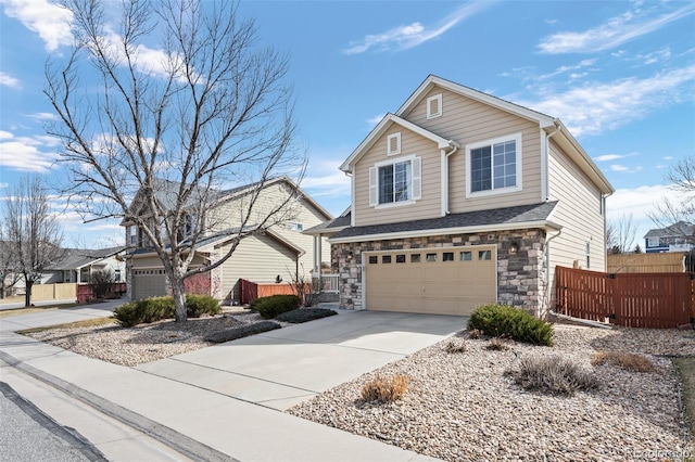 traditional home featuring concrete driveway, an attached garage, fence, and stone siding