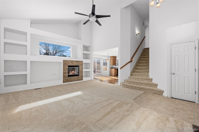 unfurnished living room featuring built in shelves, a premium fireplace, ceiling fan, stairs, and tile patterned flooring