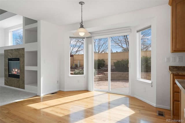 unfurnished dining area with visible vents, baseboards, built in features, light wood-style flooring, and a tile fireplace